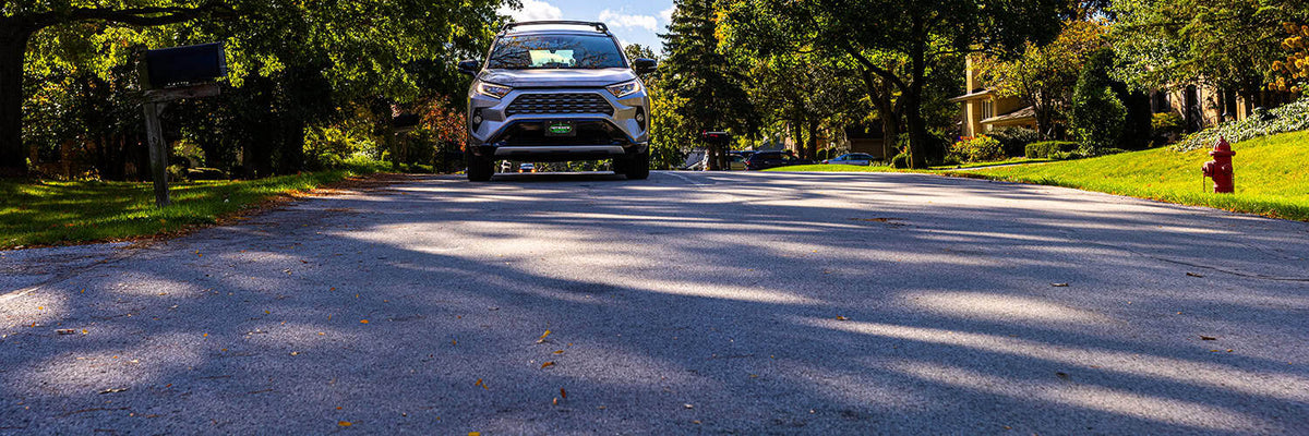 A silver SUV is parked on a paved road in a wooded outdoor setting.